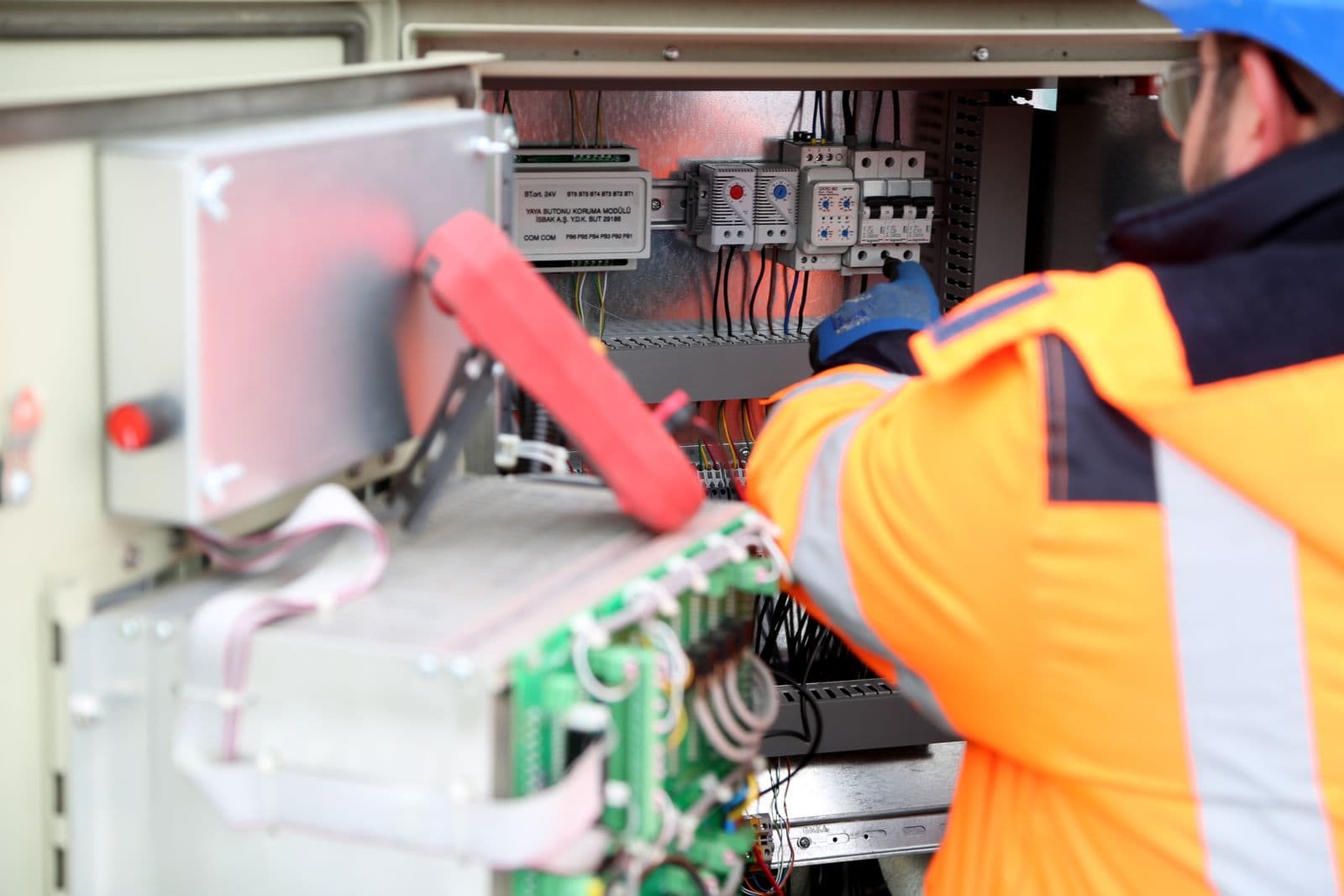 Electrician in high-visibility gear wiring a service panel