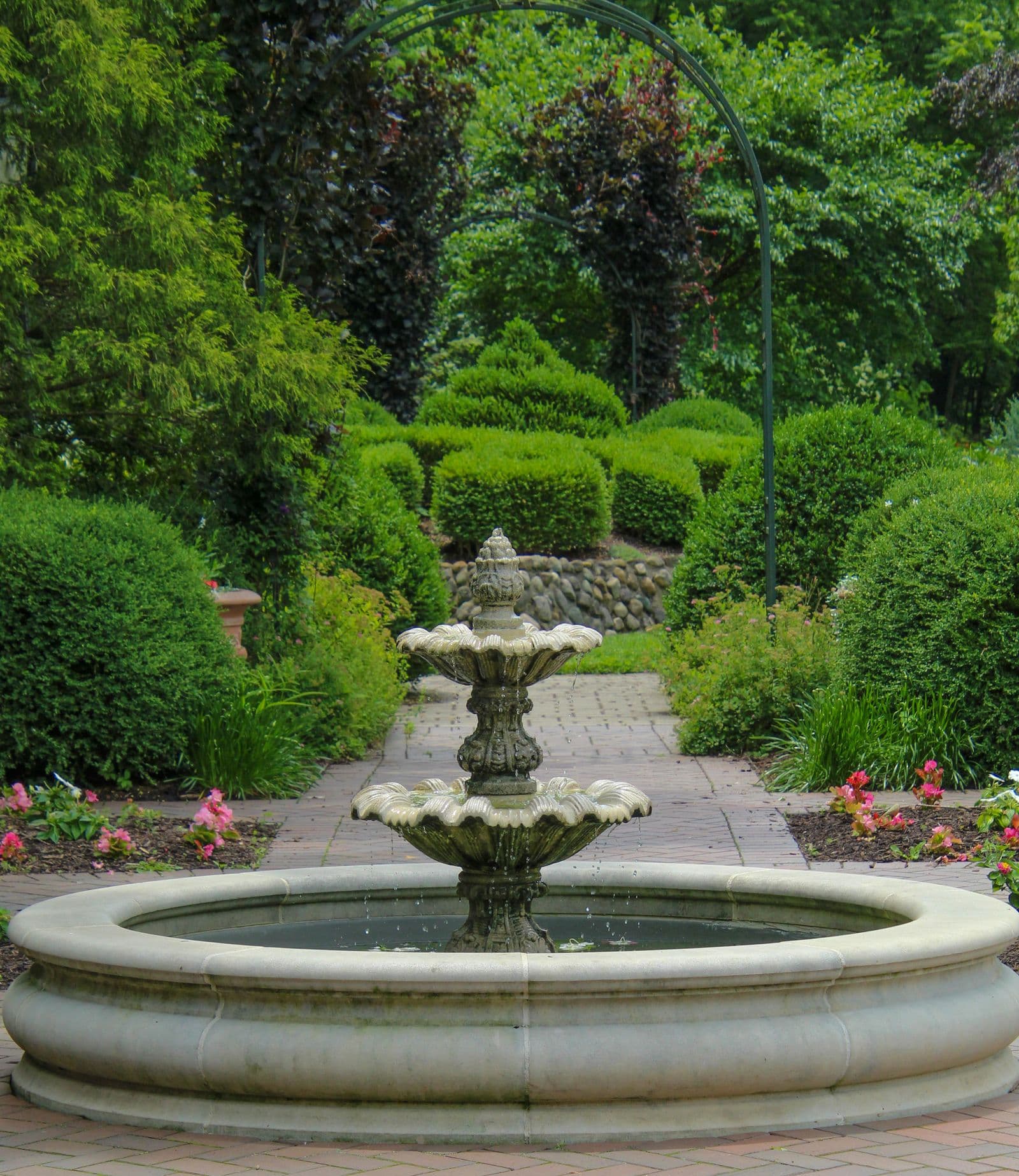 A formal garden with a stone fountain, clipped hedges and symmetrical plantings