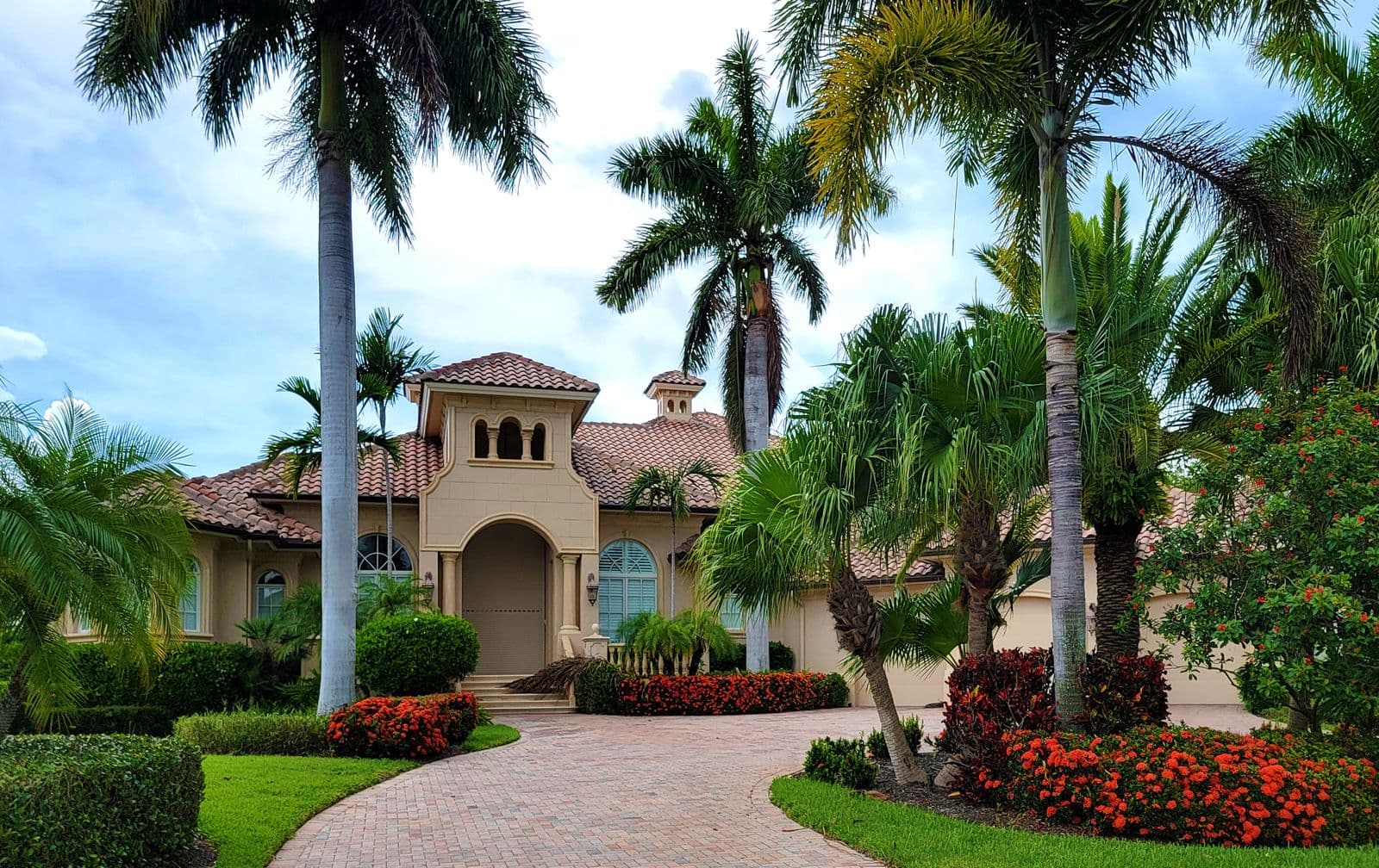 A manicured estate landscape with tall palms, layered plantings and a paved entry designed by Verdant & Stone